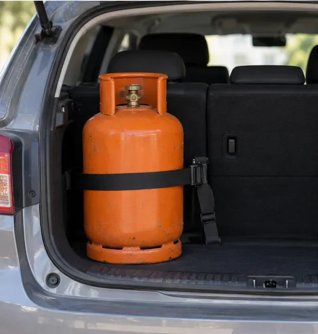 Una bombona naranja permanece vertical y sujeta con una correa dentro del maletero abierto de un coche.
