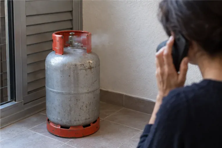 Una persona habla por teléfono manteniéndose apartada de una bombona de gas metálica colocada en vertical junto a una zona ventilada.