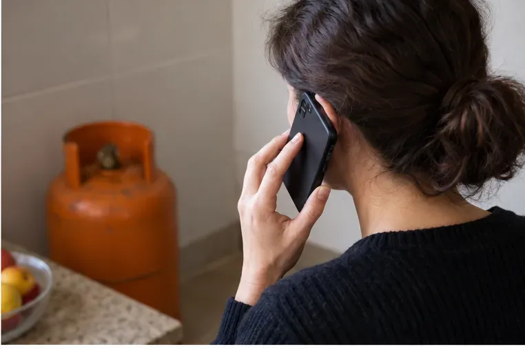 Persona llamando por teléfono desde casa con una bombona de gas al fondo para coordinar su retirada