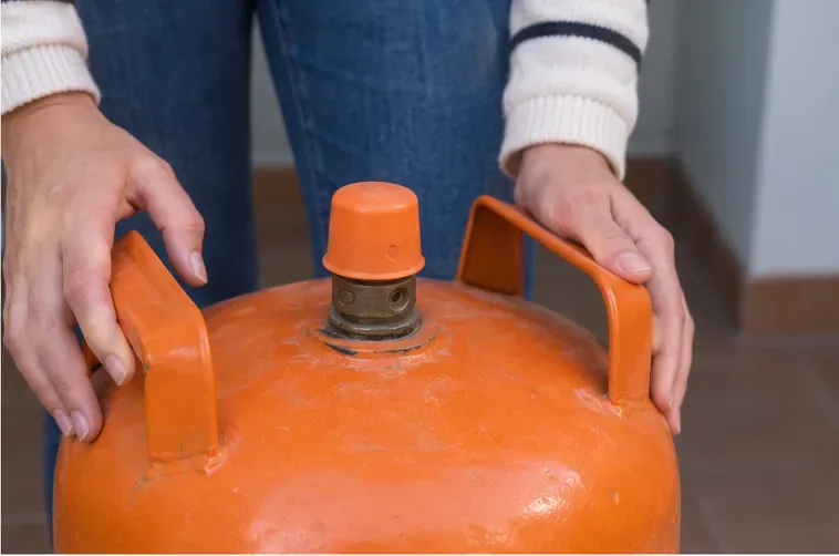 Primer plano de la parte superior de una bombona naranja con su válvula protegida por un tapón