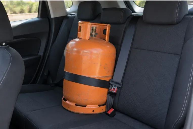 Bombona de gas colocada verticalmente y sujeta con un cinturón en el asiento trasero de un vehículo