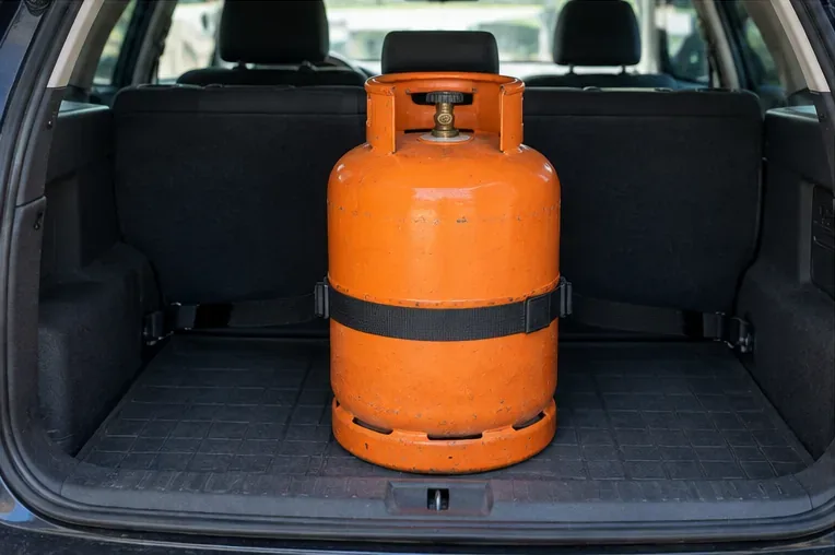 Bombona de gas colocada verticalmente y sujeta con una cincha en la zona de carga de un coche