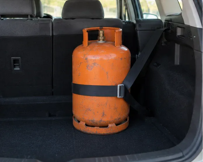 Bombona de gas colocada verticalmente y fijada con una cinta dentro del maletero de un vehículo