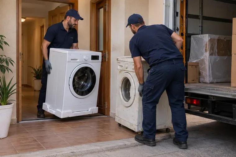 Dos repartidores entregan una lavadora nueva mientras retiran una lavadora antigua desde la entrada de una vivienda