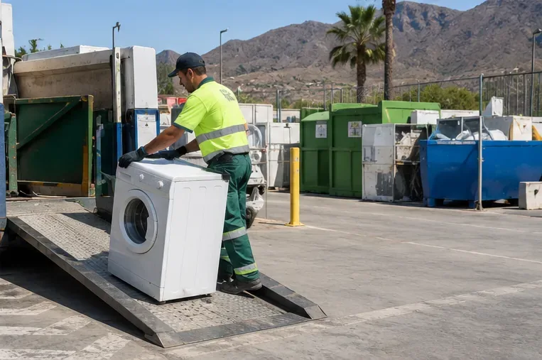 Un operario de alta visibilidad mueve una lavadora por una rampa dentro de una instalación de gestión de residuos.