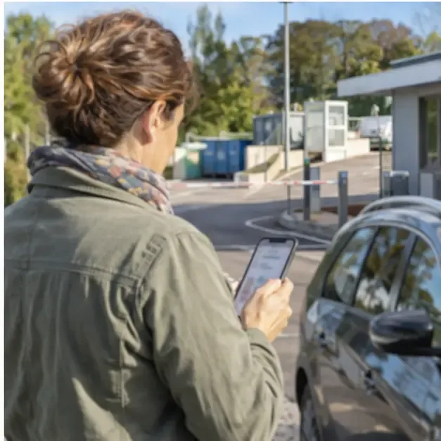 Habitante consultant les horaires sur son téléphone près d’une voiture à l’entrée d’une déchèterie