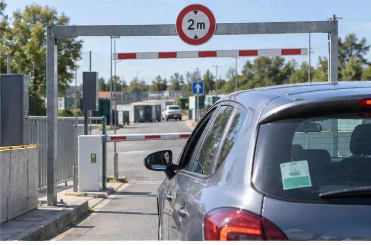 Une voiture particulière arrive à l'entrée d'une déchèterie avec un portique affichant une hauteur maximale de deux mètres