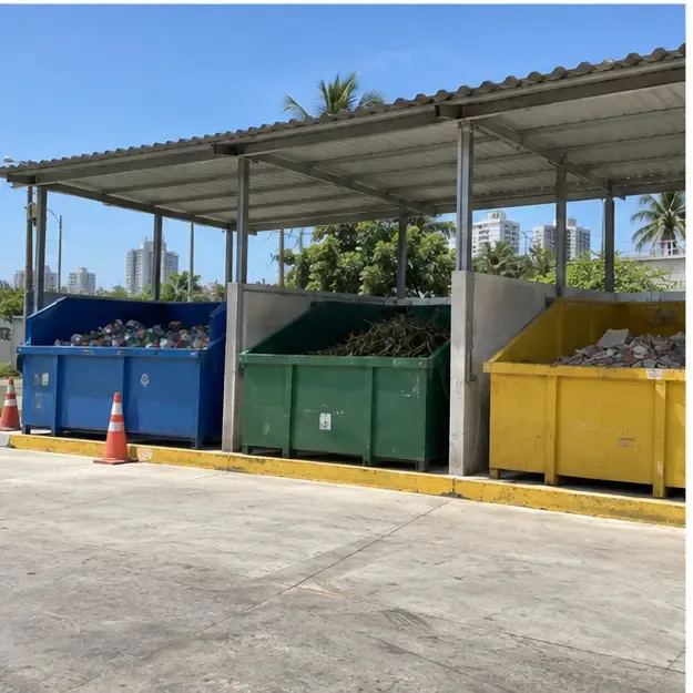 Ecoponto coberto com caçambas separadas para materiais recicláveis, galhos e resíduos de obra em uma área urbana ensolarada