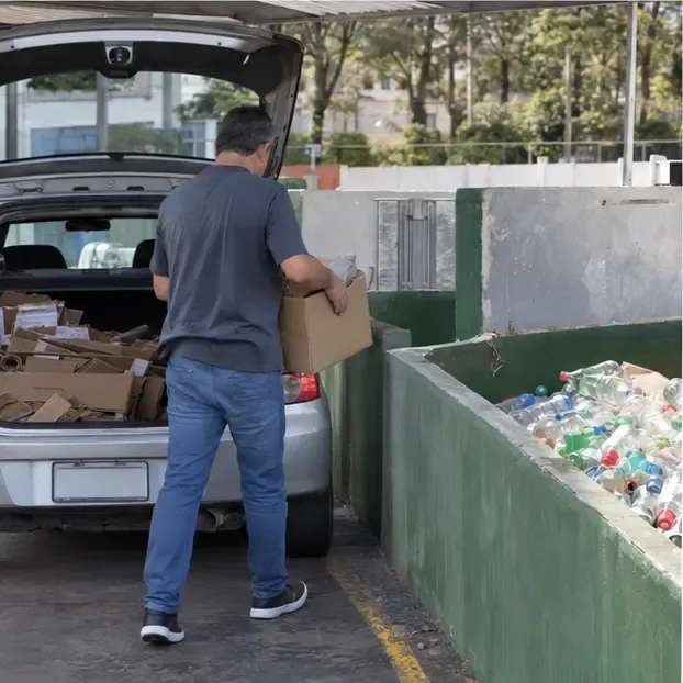 Morador retirando uma caixa de materiais separados do carro e levando-a para uma baia de coleta