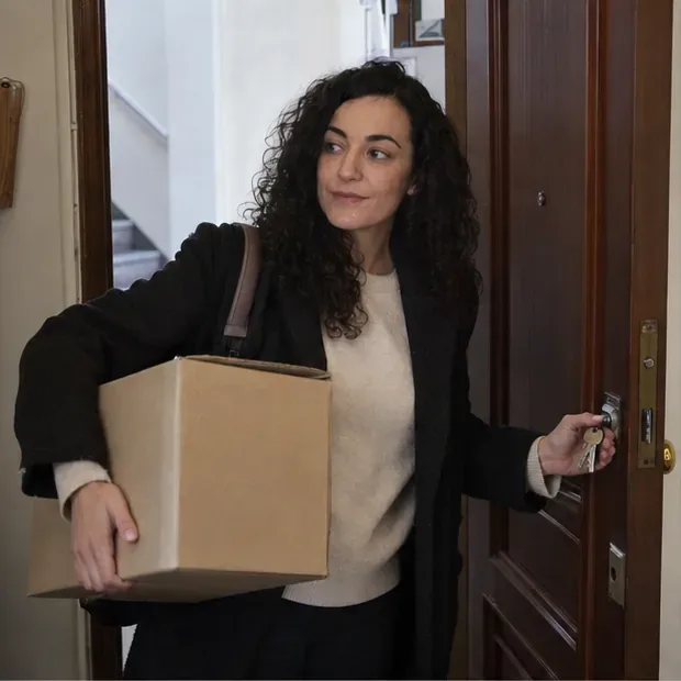 Mujer con una caja y unas llaves en la entrada de un piso al que acaba de mudarse.