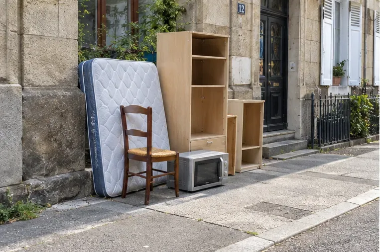 Un matelas, une chaise, une armoire démontée et un micro-ondes sont regroupés proprement devant une habitation pour un enlèvement prévu.