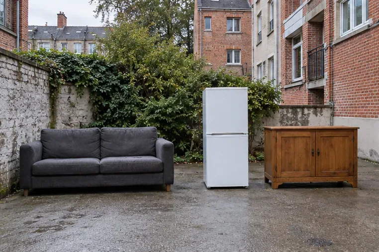 Dans une cour, un canapé, un réfrigérateur et un meuble en bois sont disposés en trois groupes séparés