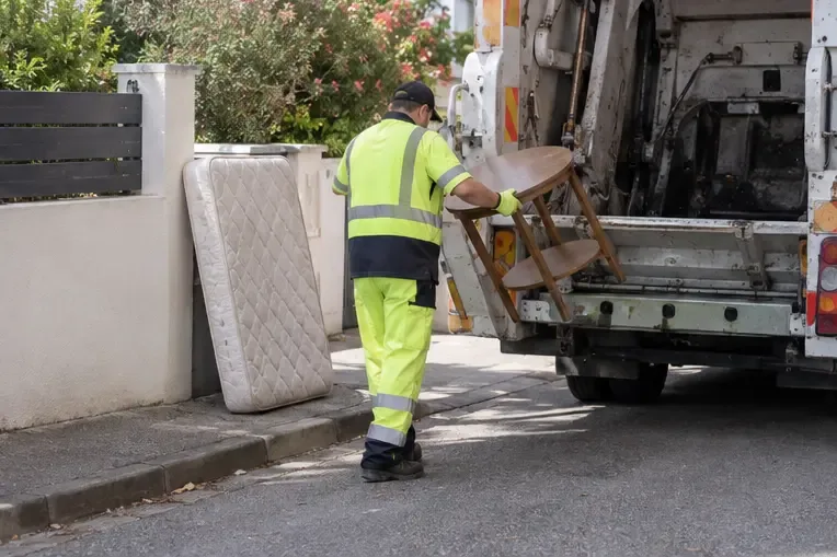 Un agent en tenue de sécurité charge une table et un matelas dans un camion depuis une rue résidentielle