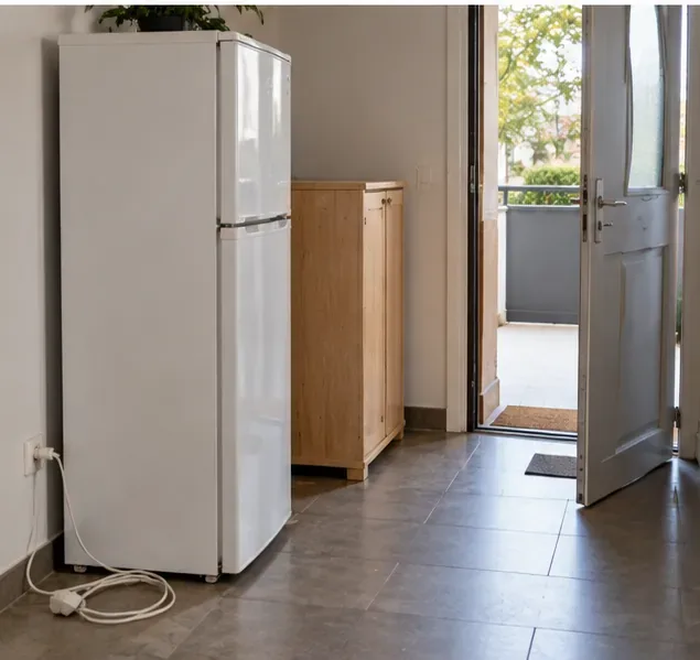 Réfrigérateur débranché et petit meuble préparés à l’intérieur d’un logement près de la sortie