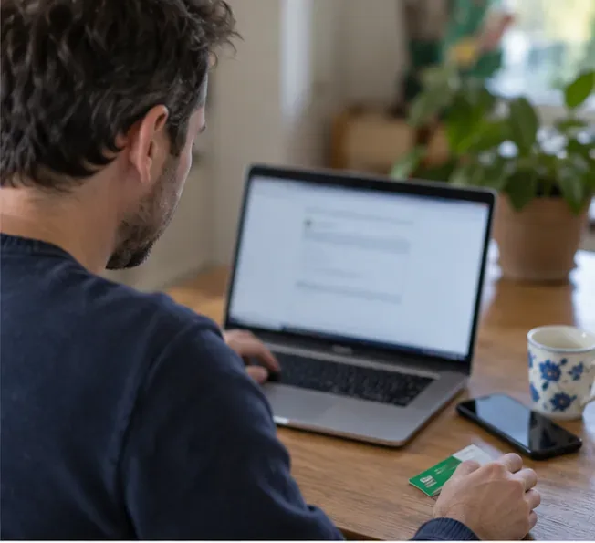 Een inwoner regelt thuis op een laptop een afspraak voor het ophalen van grofvuil en houdt zijn milieupas bij de hand.