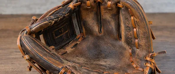 A well-used brown leather baseball glove resting open on a wooden table before cleaning