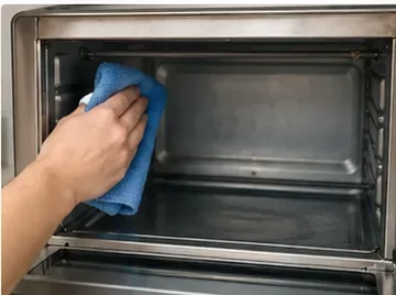 A soft cloth wiping the inside wall of a countertop toaster oven while avoiding the heating elements.