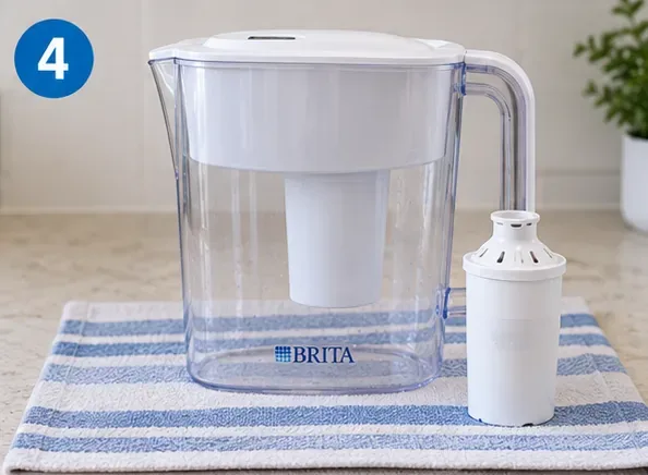 A clean reassembled Brita-style pitcher resting on a striped towel with a filter cartridge standing beside it