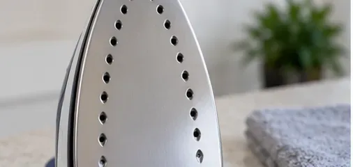 Clean metal steam-iron soleplate with open steam holes beside a folded cloth