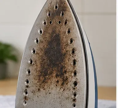 Close-up of a steam iron soleplate with a large patch of dark burnt residue around the steam holes