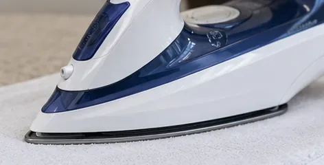 Blue-and-white steam iron gliding over a folded white scrap cloth after cleaning