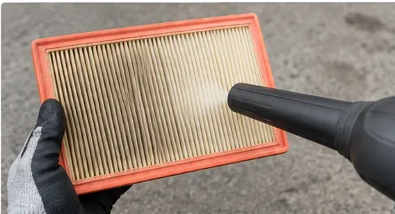 A vacuum nozzle held near the pleated surface of a rectangular engine air filter