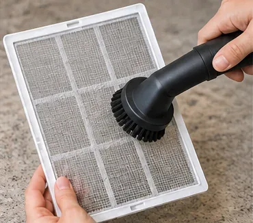 A soft vacuum brush lifting loose dust from a removable dehumidifier mesh filter