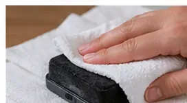 A hand pressing a damp dry-erase eraser against a clean white towel