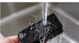 A dark dry-erase eraser pad receiving a final rinse under a faucet