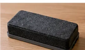 A rectangular black dry-erase board eraser resting on a wooden table for inspection