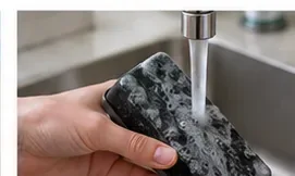 A hand rinsing a dark dry-erase eraser pad under clean running water