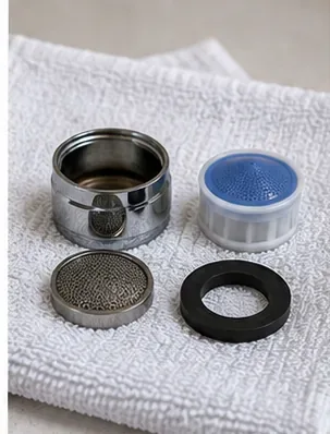 A disassembled faucet aerator with chrome housing, metal screen, blue plastic insert, and black gasket arranged on a towel.