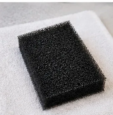 A cleaned black filter sponge rests briefly on a clean towel while remaining damp.