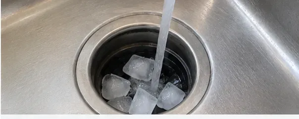 Cold tap water running directly into a garbage disposal that contains ice cubes.