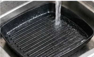 Clean water rinsing soap and loosened residue from the channels of a dark grill pan