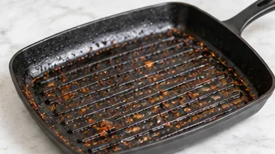 A dark ridged grill pan with browned food residue resting on a countertop after cooking