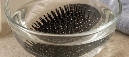 A black paddle hairbrush submerged in a clear glass bowl of water for the soaking step