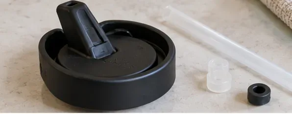 A black straw cap, clear straw, and small removable seal parts laid out on a kitchen counter before cleaning