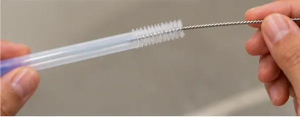 A narrow straw brush being passed through the inside of a clear reusable drinking straw