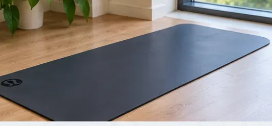 A dark yoga mat lies flat indoors near a window while air-drying away from direct sunlight.