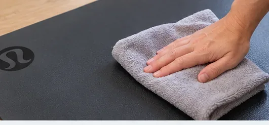 A hand presses a clean dry towel against a dark yoga mat to remove surface moisture.