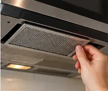 A hand sliding a clean, dry grease filter back into its slot under an over-the-range microwave.