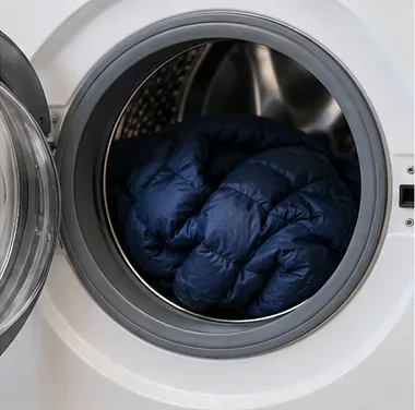 A navy down jacket placed loosely inside the drum of a front-loading washing machine.