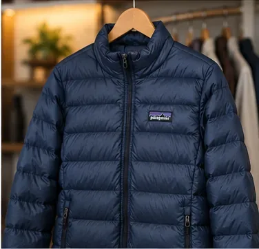 A fully lofted navy Patagonia down jacket hanging freely on a wooden hanger after cleaning.