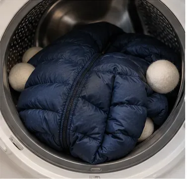 A navy down jacket tumbling inside a dryer with soft round balls spaced around the garment.