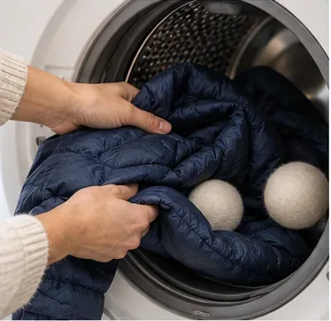 A wet navy down jacket being moved carefully into a front-loading dryer.