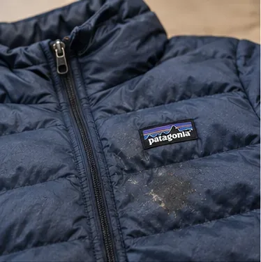A navy Patagonia down jacket with visible dirt on the front baffles before cleaning.