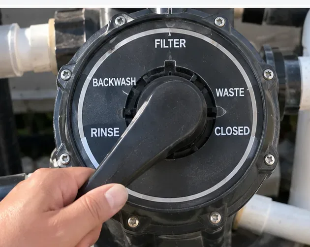 Close-up of a pool multiport valve with a hand near the handle and the Rinse label visible.