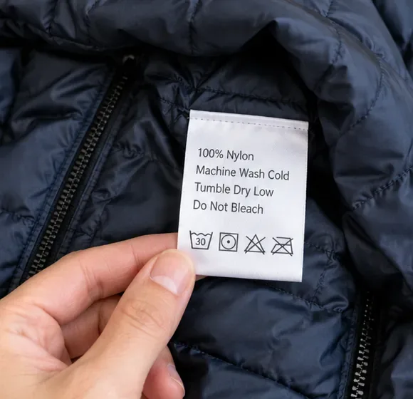 A hand holding the care label inside a navy puffer jacket, showing machine-wash and low-tumble-dry instructions