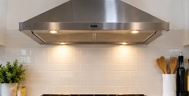 A stainless-steel wall-mounted range hood installed above a clean white tile backsplash
